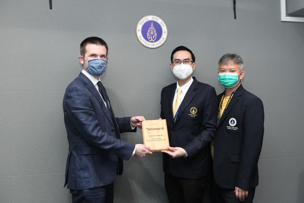 man in mask presents a plaque to a man and woman both wearing masks