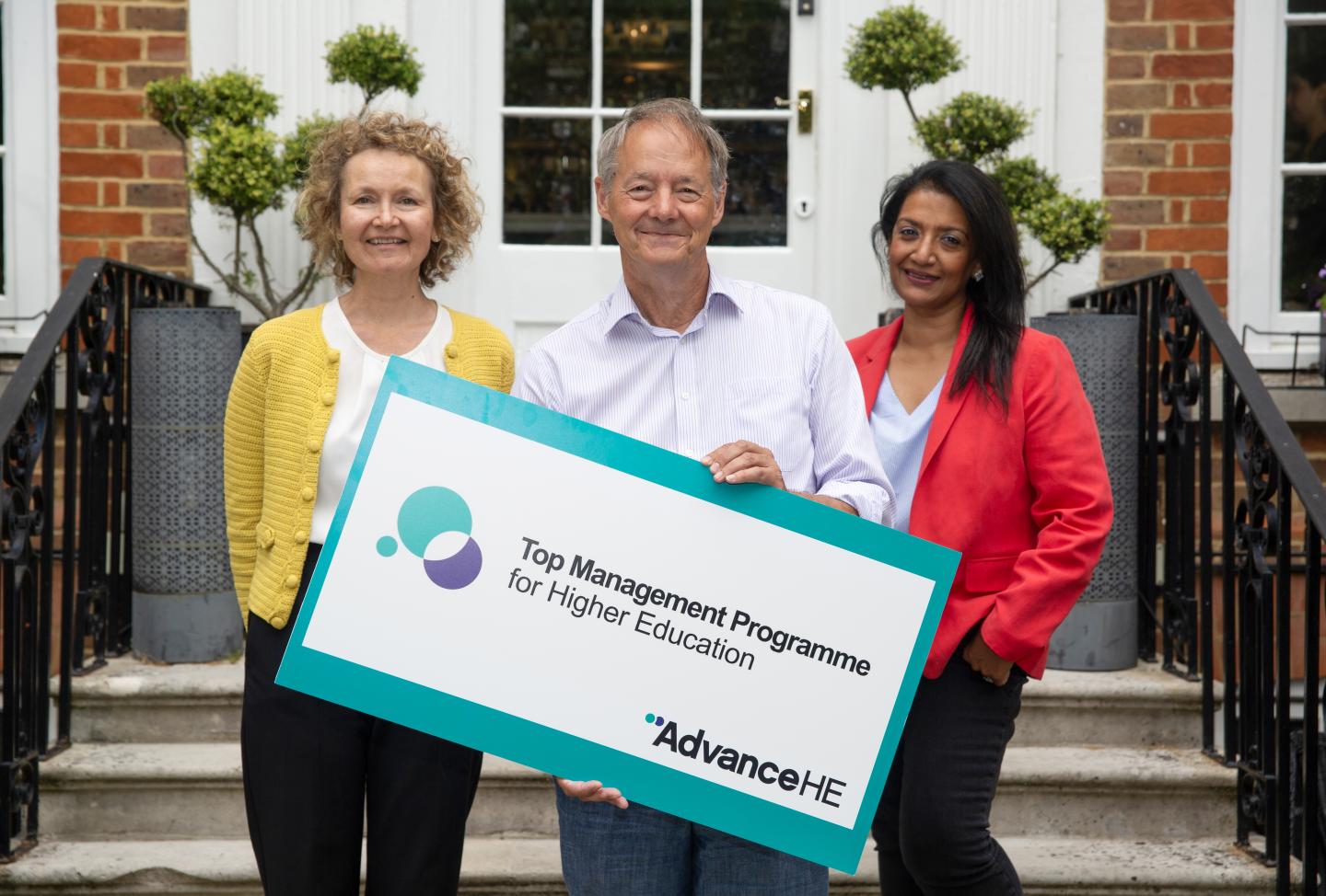 Two women and a man hold a sign saying Top Management Programme