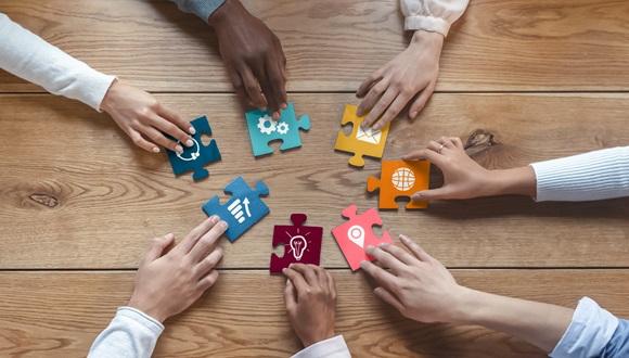 Hands of diverse coworkers putting colourful puzzle pieces together representing collaboration
