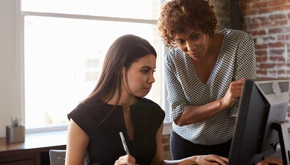 Two women look at a desktop computer together