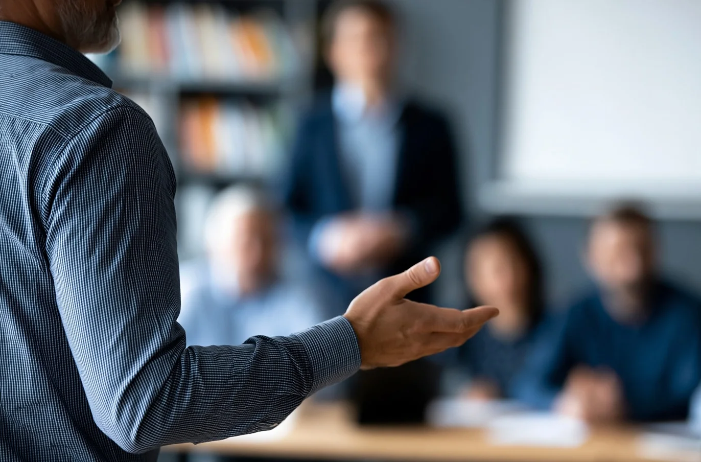 Faceless business trainer facilitating a leadership development workshop for a group of managers in a corporate training room, defocused training environment in background