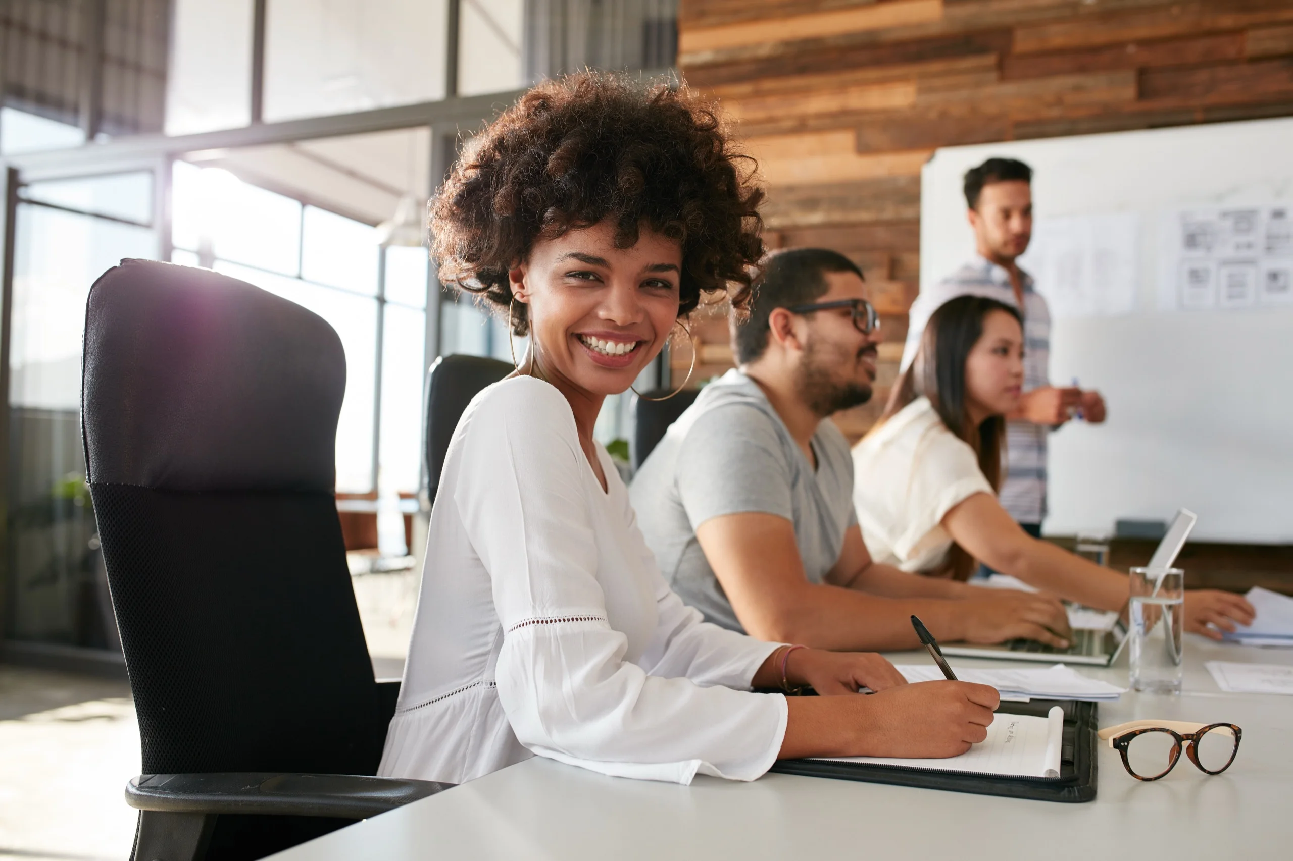 Group of people working around a desk with a woman directly looking into the camera