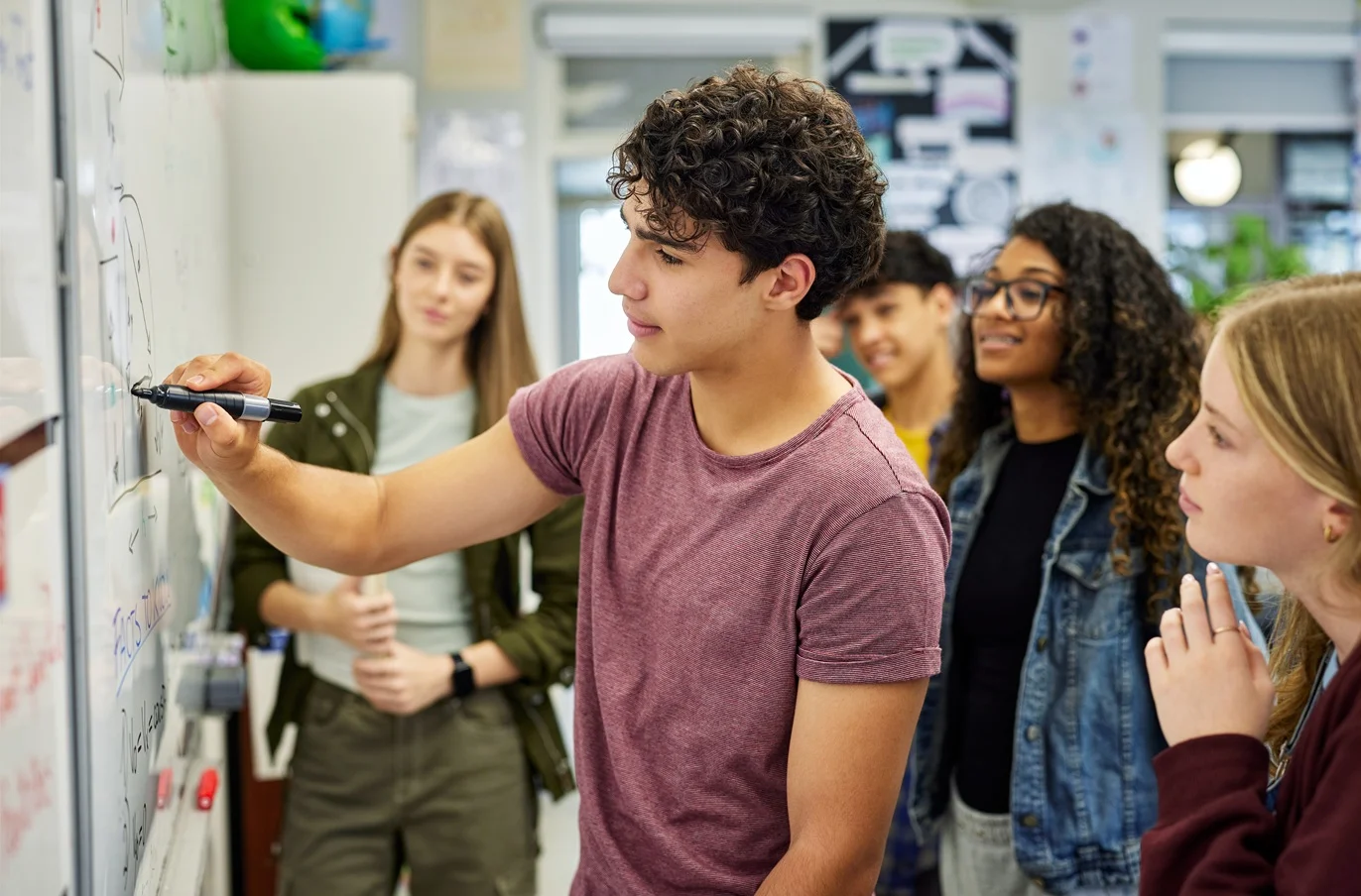 Students gathered around a white board solving a problem 